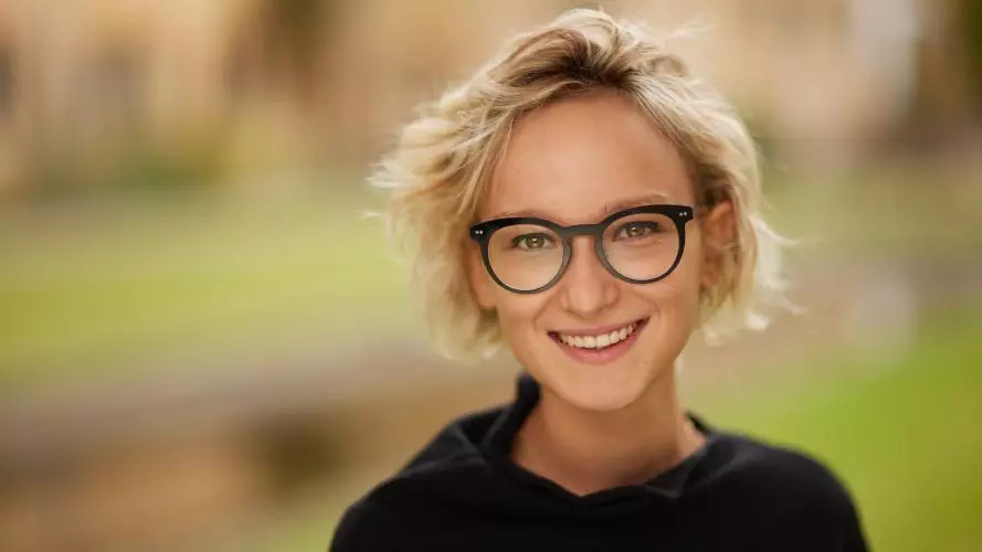 Smiling woman with short blond hair and dark rimmed glasses, wearing a black jumper