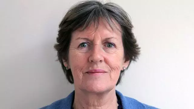 Woman with short dark grey hair looking directly at the camera and wearing a dark blue shirt