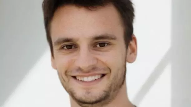 Michael Ganslmeier has short dark hair, dark eyes and dark facial hair. He is wearing a black t-shirt and smiling. 