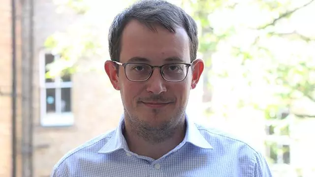 Man with short brown hair who is smiling and wearing dark rimmed glasses