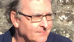 Paul Harnett  has short grey hair and is wearing glasses. 