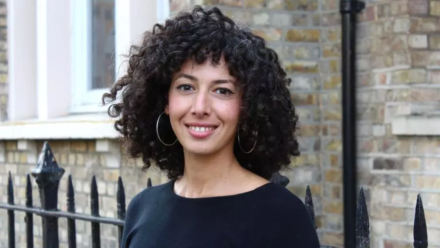 Rana Khazbak has curly black hair, wearing a black top with big silver hoop earrings smiling at the camera.