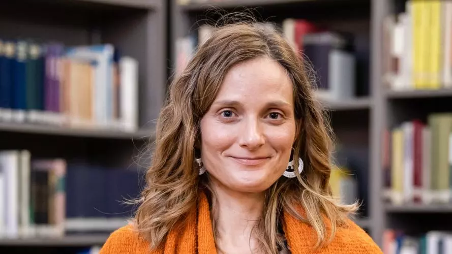 Woman with light brown hair who is smiling and wearing an orange shawl