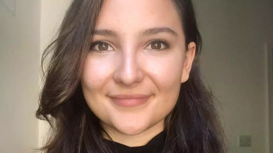 Stephanie has long brown wavy hair and is smiling at the camera. She's wearing a black jumper. 