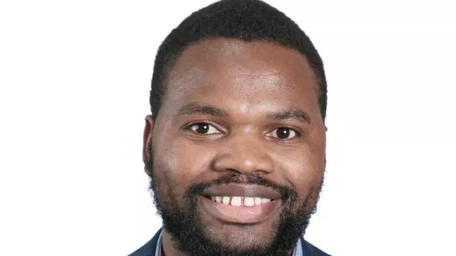 Dr Siyanai Zhou is wearing a dark blue with stripes jacket, with a blue shirt with short afro hair, smiling at the camera.