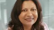 Yvonne has shoulder-length brunette hair. She is wearing a pink blazer and pearl necklace