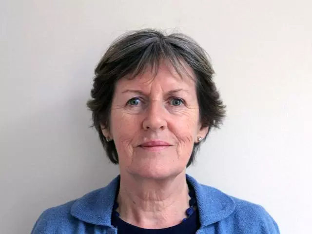 Woman with short dark grey hair looking directly at the camera and wearing a dark blue shirt
