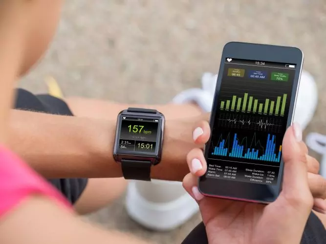 A runner wearing a smartwatch tracking their fitness statistics. They are holding their smartphone next to their wrist, looking at more detail on a fitness app.