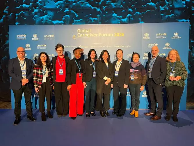 A group of ten, smartly dressed people stand in front of a sponsorship banner at the Global Caregiver Forum in Madrid