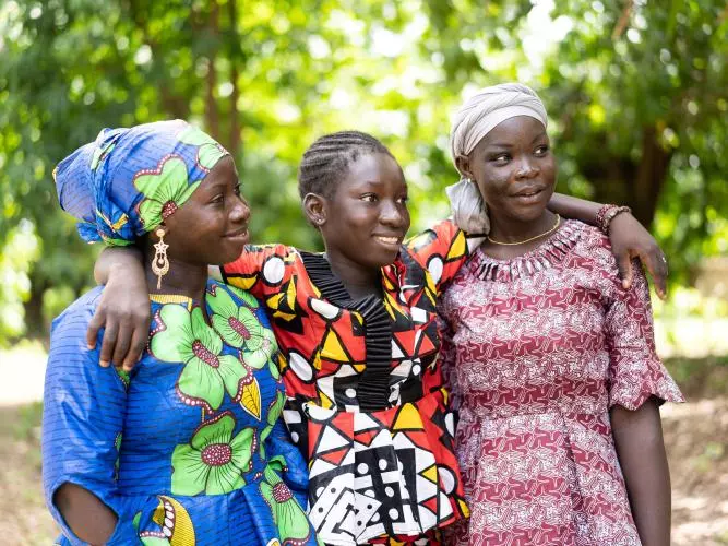 Three adolescent girls in colourful outfits. The girl in the middle has her arms around the shoulders of her friends either side. Credit: stock.adobe.com / Riccardo Niels Mayer