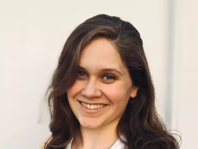 Anja is smiling widely at the camera. She has long dark hair and is wearing a sleeveless white blouse. 