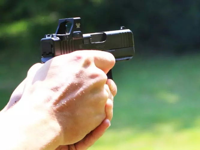 A man's hand holds out a handheld shotgun, aiming at nothing