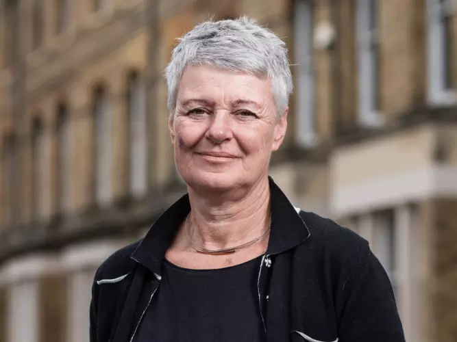 Jane Barlow is wearing a black top and jacket, with short gray hair, smiling for the camera.