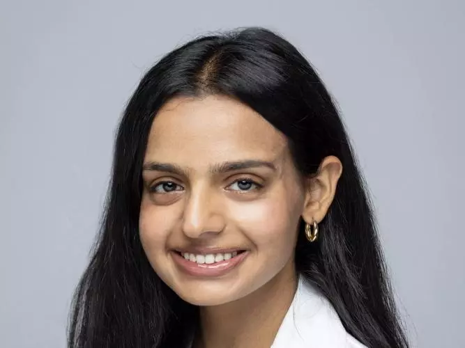 kapoor nandini wears a lab coat, has long dark hair and is smiling in front of a plain background