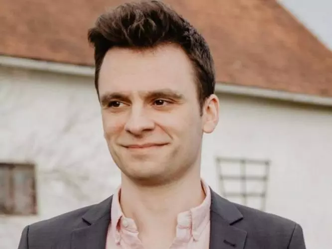 Michael Ganslmeier a DSPI doctoral researcher is smiling while wearing a dark grey suit and a salmon shirt.