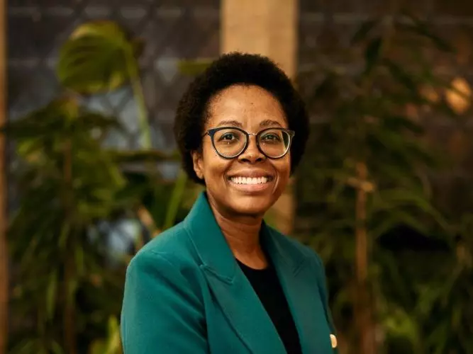 Zamakhanya Makhanya has afro hair, with black rimmed glasses, weating a green jacket smiling at the camera.