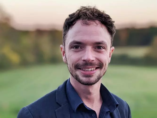 Hal Cooper, with short brown hair, is wearing a dark blue shirt and jacket, smiling at the camera