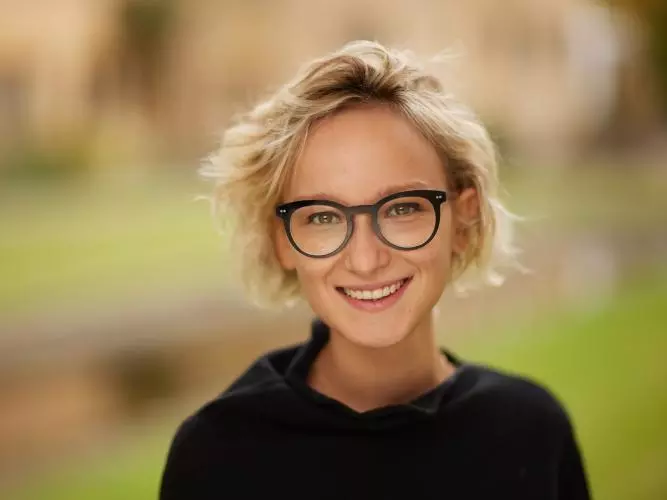 Smiling woman with short blond hair and dark rimmed glasses, wearing a black jumper