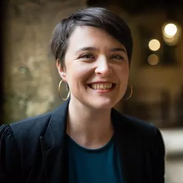 Dr Aoife O’Higgins is wearing a navy blue jacket and top. She has short dark hair, large hoop earrings and is smiling at the camera 