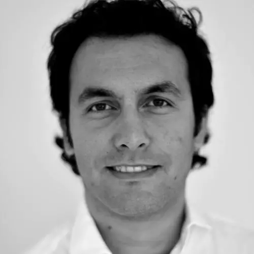A black and white photo of Erdem Yörük, who has curly dark hair and is wearing an open-collared white shirt