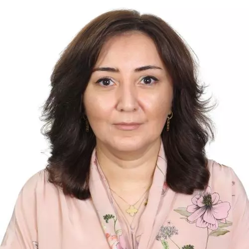 Bahija Aliyeva wears a peach blouse with a floral pattern. She had shoulder-length dark brown hair and is on a plain white background.