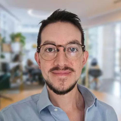 Hernando has short dark hair and a beard, and is wearing glasses. He is wearing a pale blue shirt.