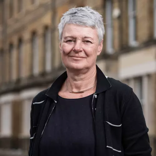 Jane Barlow is wearing a black top and jacket, with short gray hair, smiling for the camera.