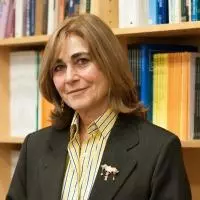 Jacqueline Bhaba is wearing a striped yellow shirt and blazer, standing in front of bookshelves