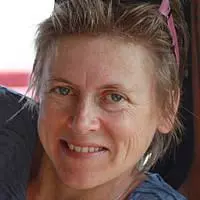 Woman with light brown hair who is smiling and has pink rimmed sunglasses on her head