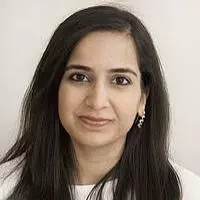 Maheen has long dark straight hair. She is wearing a white top. 