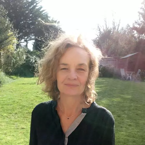 Elaine Chase has short blonde hair and is wearing a black top. She is standing in a grassy area.