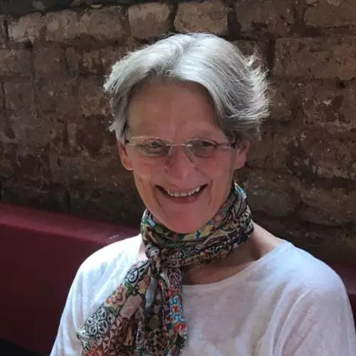 Professor Ward is looking slightly downwards and smiling. She has short grey hair and is wearing rimless glasses, a patterned scarf and a white t-shirt. 