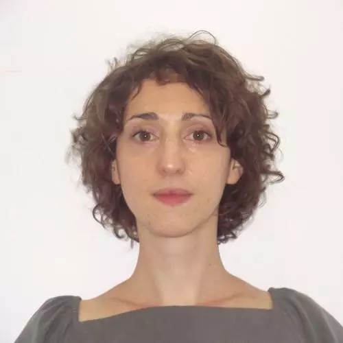 A headshot of Ilka Vari-Lavoisier. She has short curly brown hair. She is standing face-on to the camera, wearing a square-necked grey top with puffed sleeves.