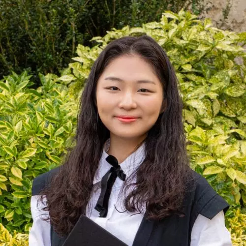 Jinseo Kim is wearing graduation gown, with dark shoulder length hair smiling at the camera.