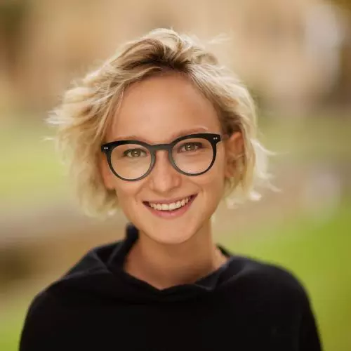 Smiling woman with short blond hair and dark rimmed glasses, wearing a black jumper