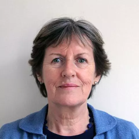 Woman with short dark grey hair looking directly at the camera and wearing a dark blue shirt