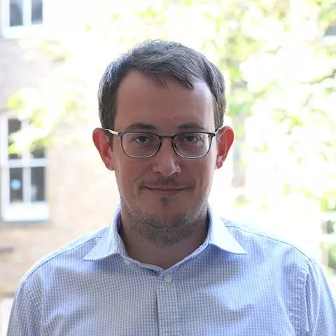 Man with short brown hair who is smiling and wearing dark rimmed glasses