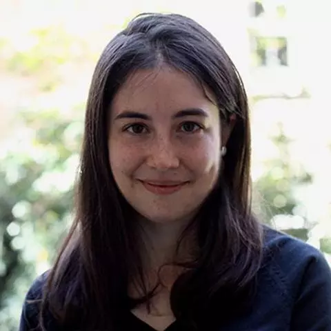 Paloma has long dark hair, is smiling at the camera and wearing a black top with navy blue jacket. 