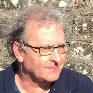 Paul Harnett  has short grey hair and is wearing glasses. 