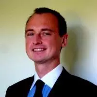 Pavelov has short brown hair. He is wearing a blue shirt with a white collar, dark tie and blazer