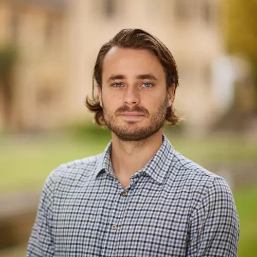 Roland has brown hair and beard, and is wearing a white checked shirt