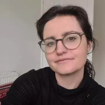 Rosemary has long dark hair and brown eyes. She is wearing a black top and round glasses. Her hair is tied back into a ponytail. 