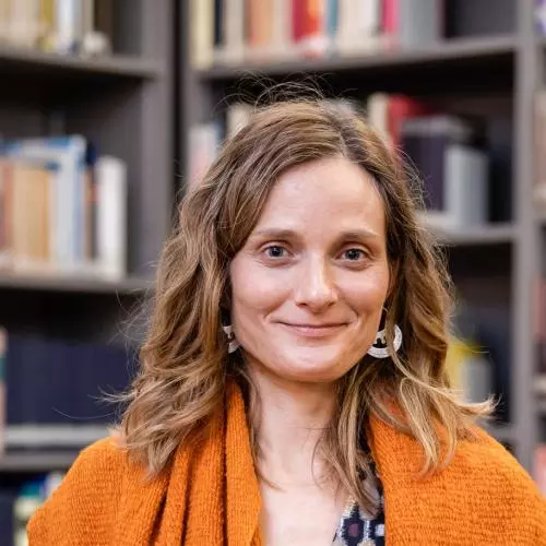 Woman with light brown hair who is smiling and wearing an orange shawl