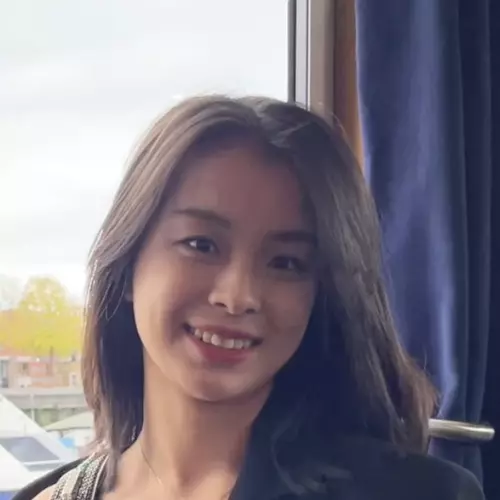 Yaxin has long dark hair. She is standing in front of a window and smiling. 