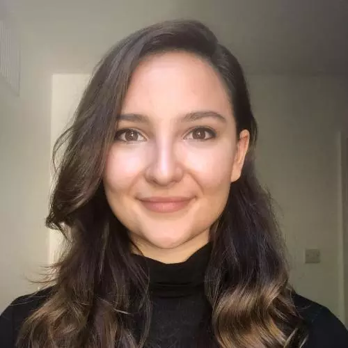 Stephanie has long brown wavy hair and is smiling at the camera. She's wearing a black jumper. 