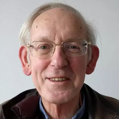 Smiling man with short grey hair and wearing gold rimmed glasses.