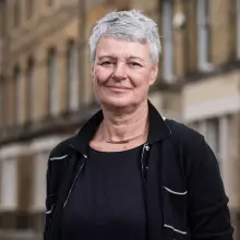 Jane Barlow is wearing a black top and jacket, with short gray hair, smiling for the camera.
