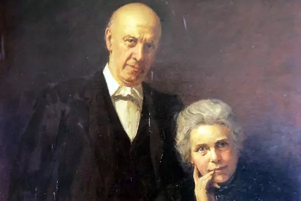 the Barnetts: A tall bald man wearing a black suit with white shirt,  a lady with grey hair is resting her chin on her hand
